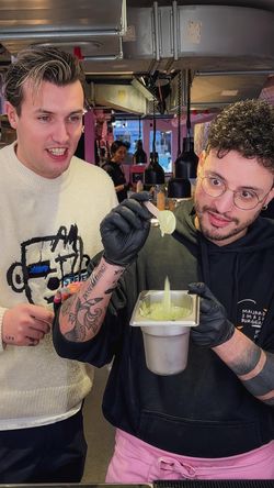 Two people at Maijard Smashburgers preparing food with black gloves and sauce in a busy burger restaurant kitchen.