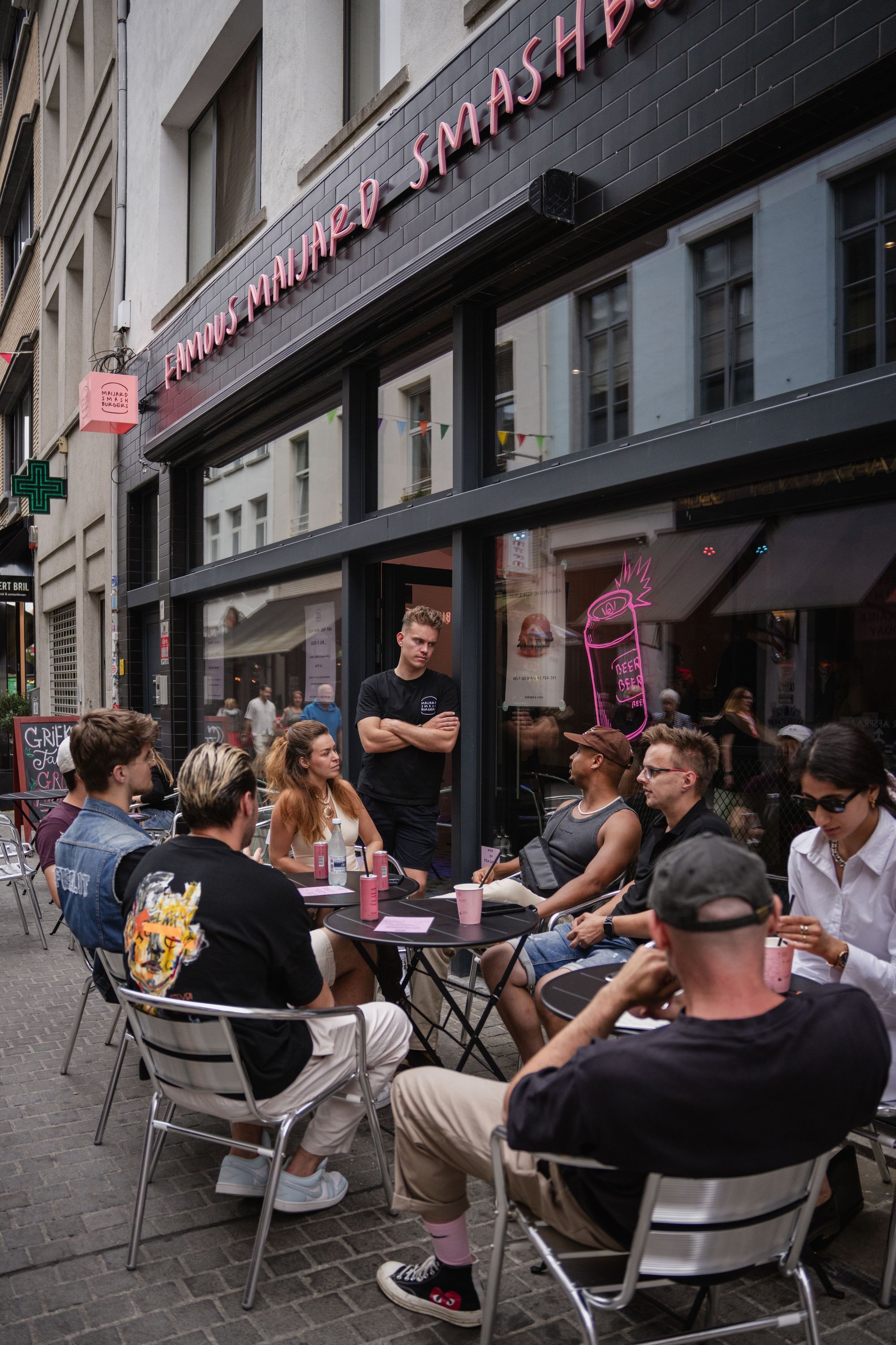 Customers sitting outside Maijard Smashburgers, enjoying drinks and the casual dining atmosphere on a city street.