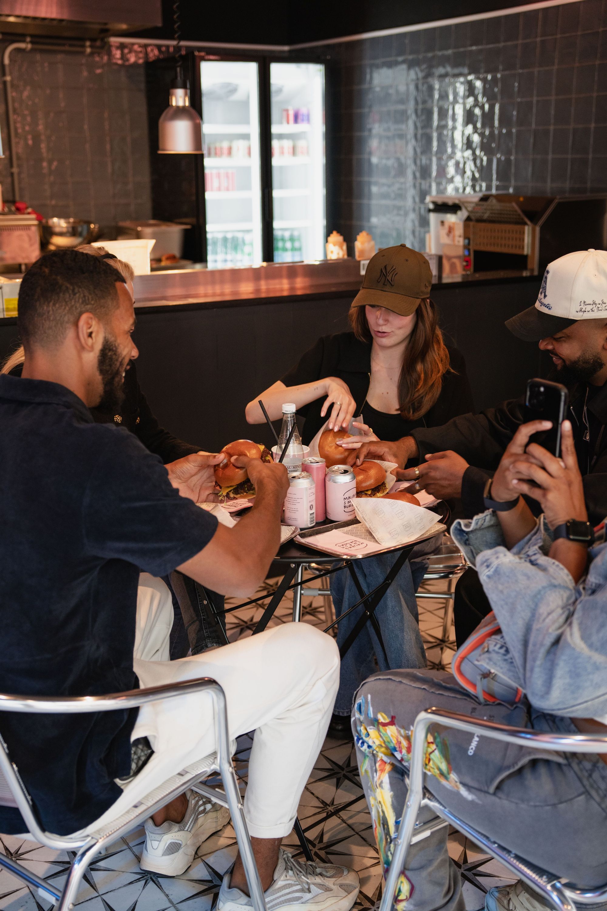 Group of people sitting around a small table enjoying homemade smash burgers and drinks at Maijard Smashburgers.