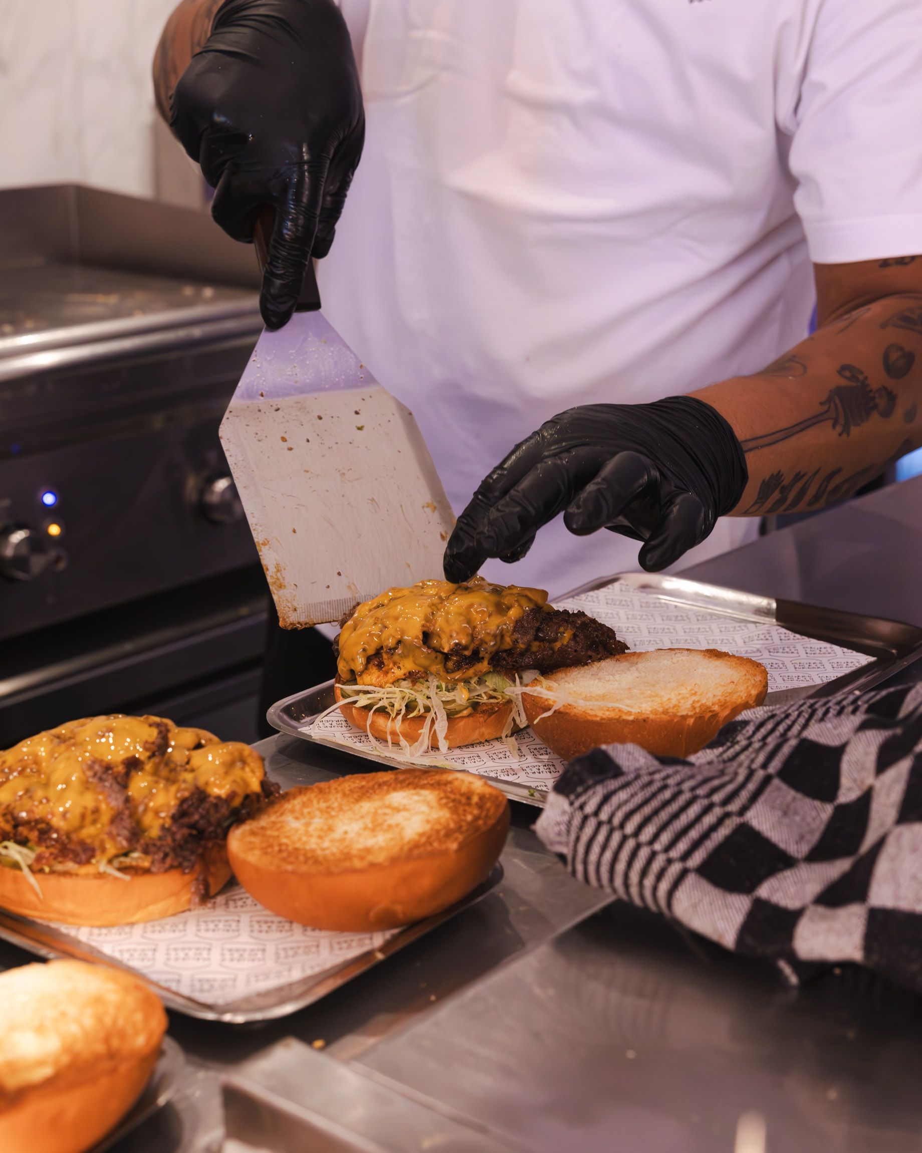Burger restaurant kitchen with chef assembling homemade smash burgers topped with melted cheese on toasted buns.