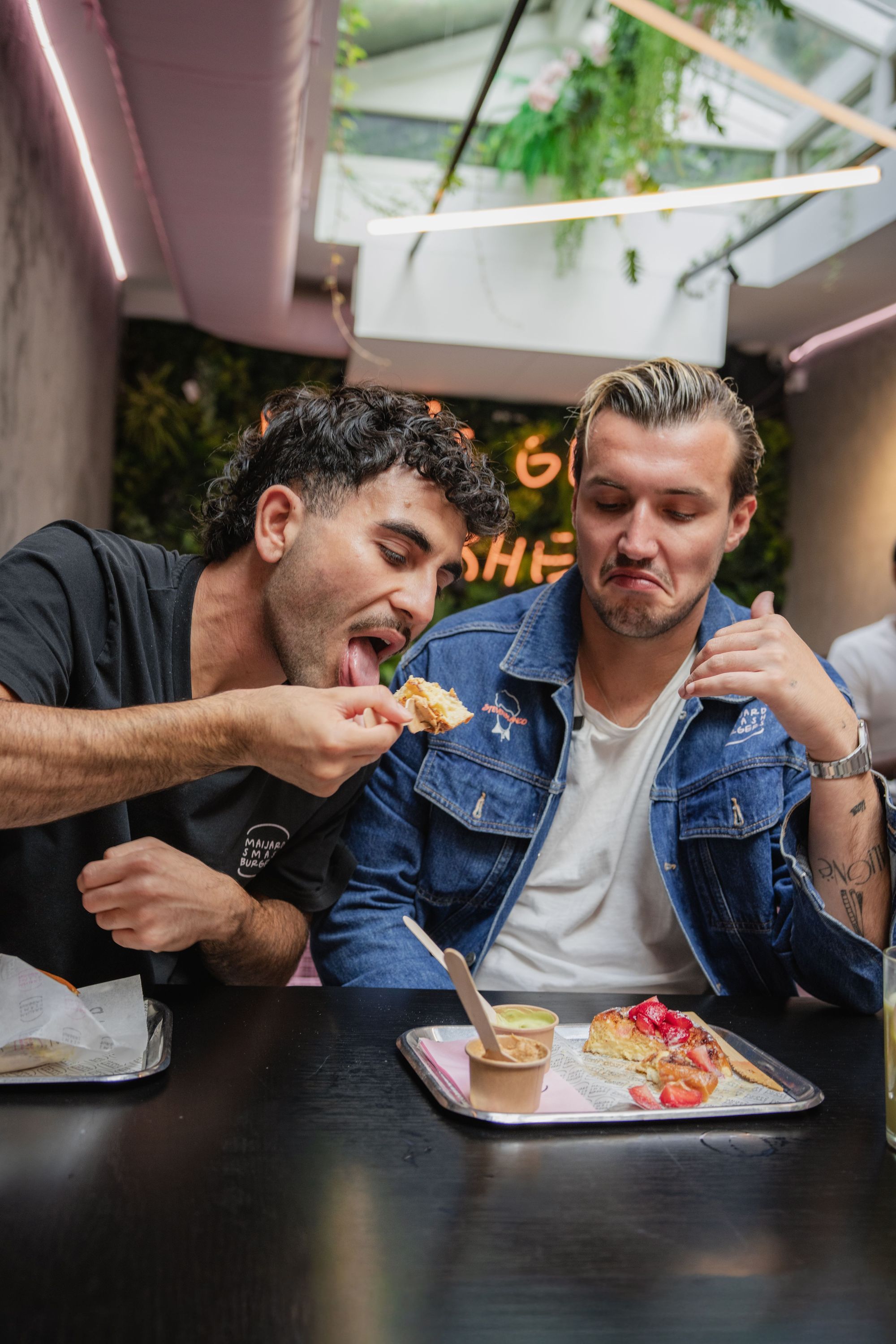 Two men eating at Maijard Smashburgers with trays holding homemade burgers and sauces on a black table