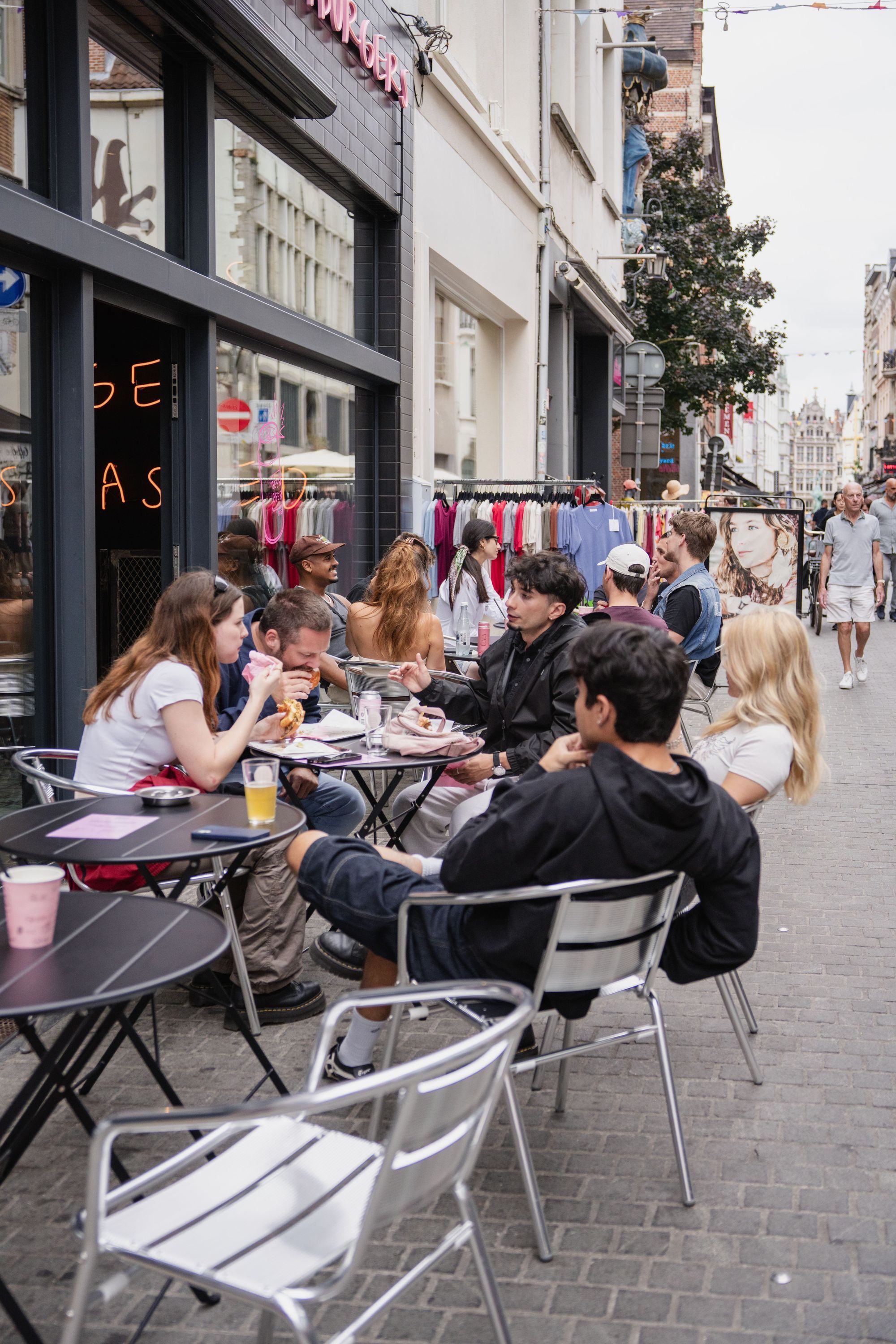 People sitting at outdoor tables enjoying burgers and drinks in front of Maijard Smashburgers burger restaurant in Amsterdam.