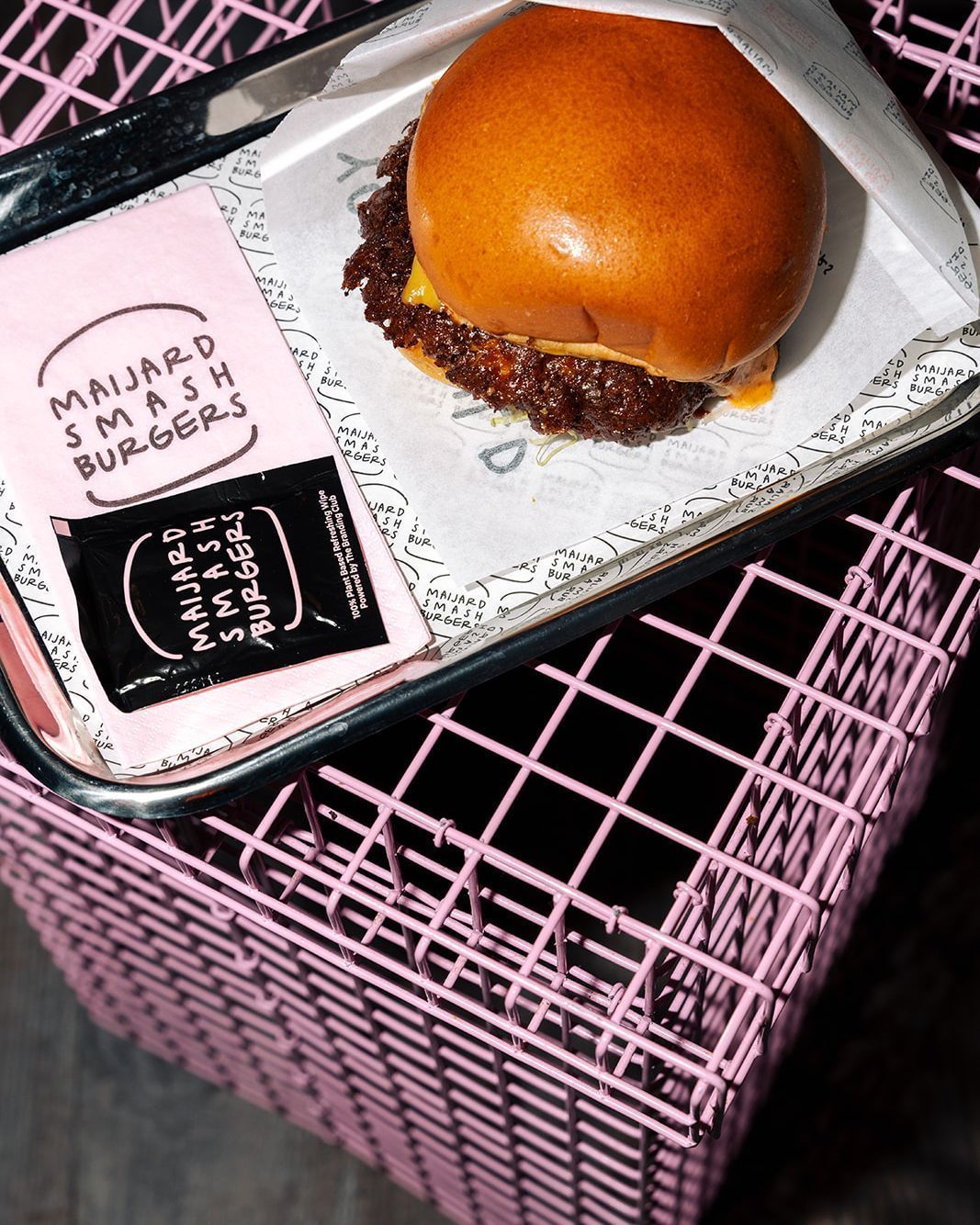 A smash burger served on branded Maijard Smashburgers paper in a tray on a pink wire rack at the Amsterdam burger bar.