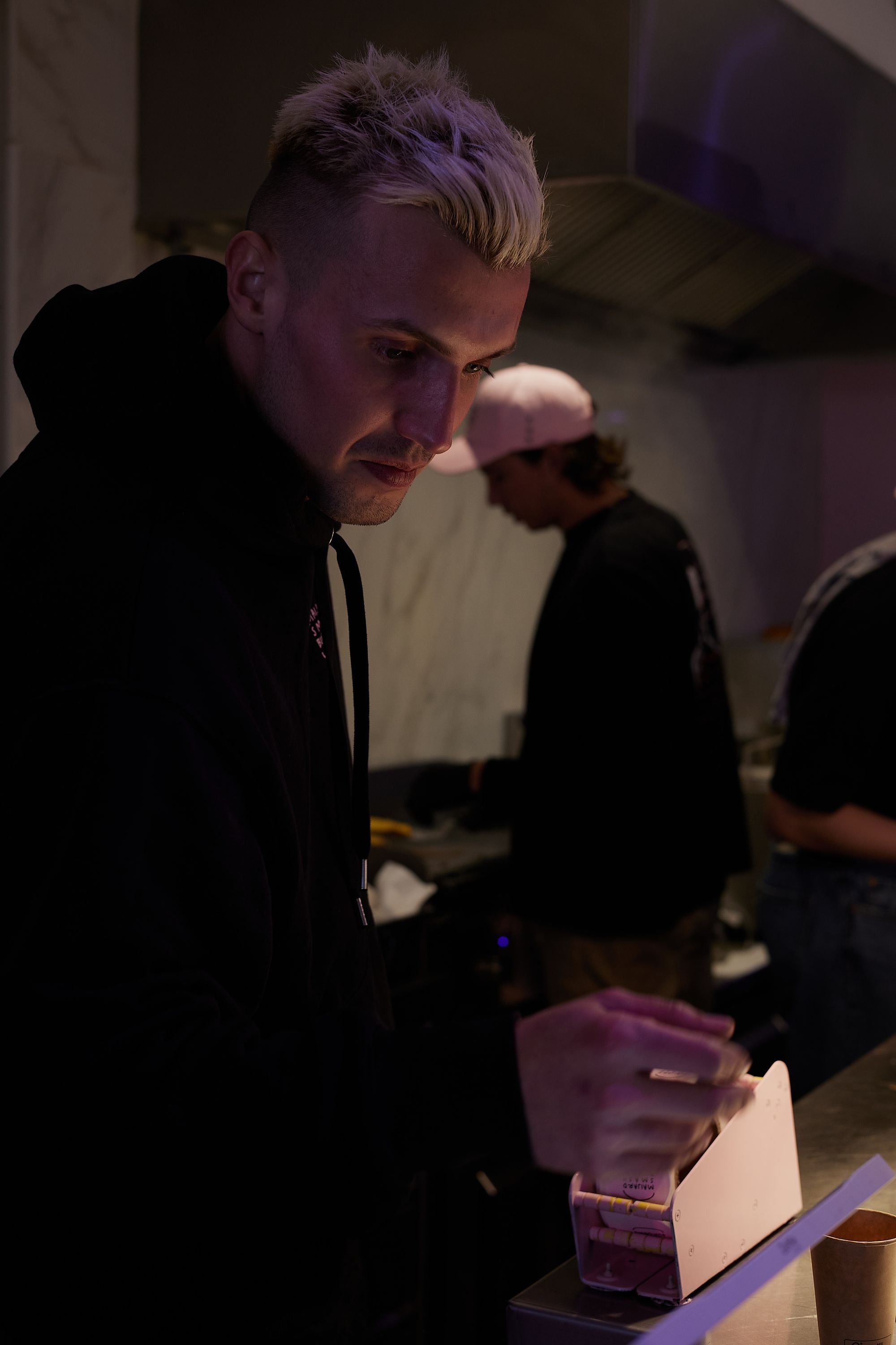 Person inside Maijard Smashburgers preparing or handling items at the counter in a dimly lit kitchen area.