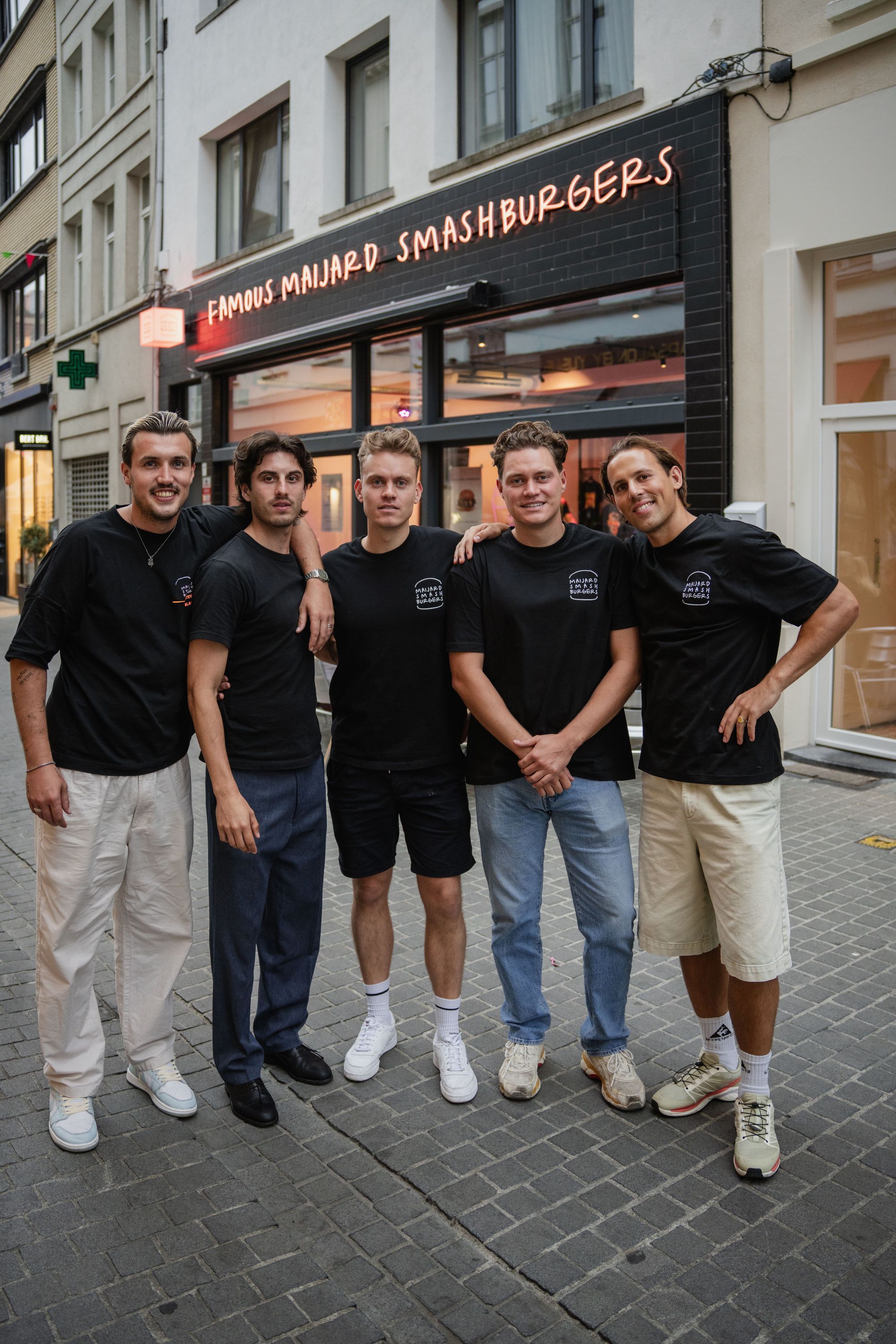 Five staff members standing outside Maijard Smashburgers burger restaurant in Amsterdam on a cobblestone street.