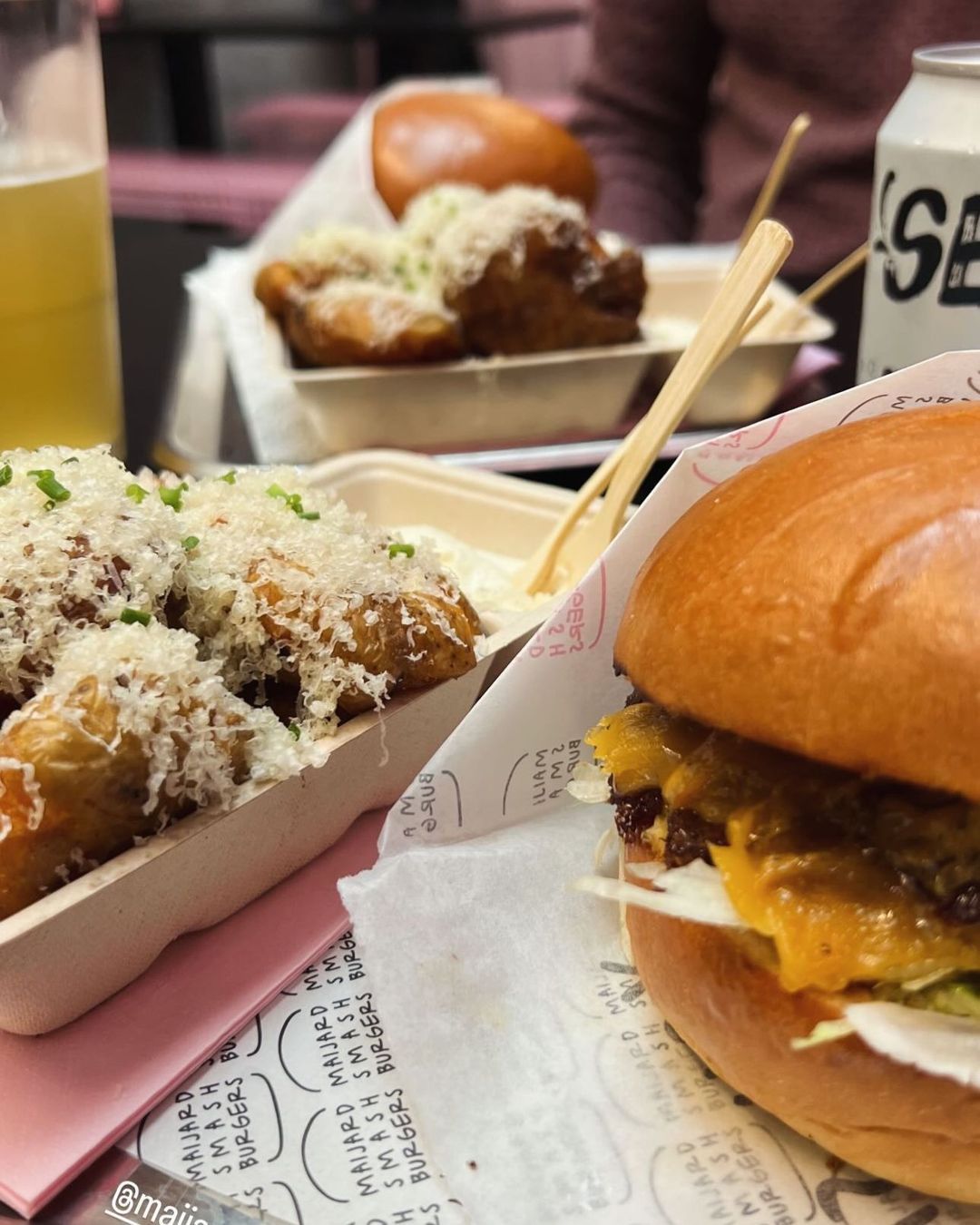 Close-up of a homemade burger with melted cheese and a container of fries topped with grated cheese at Maijard Smashburgers.