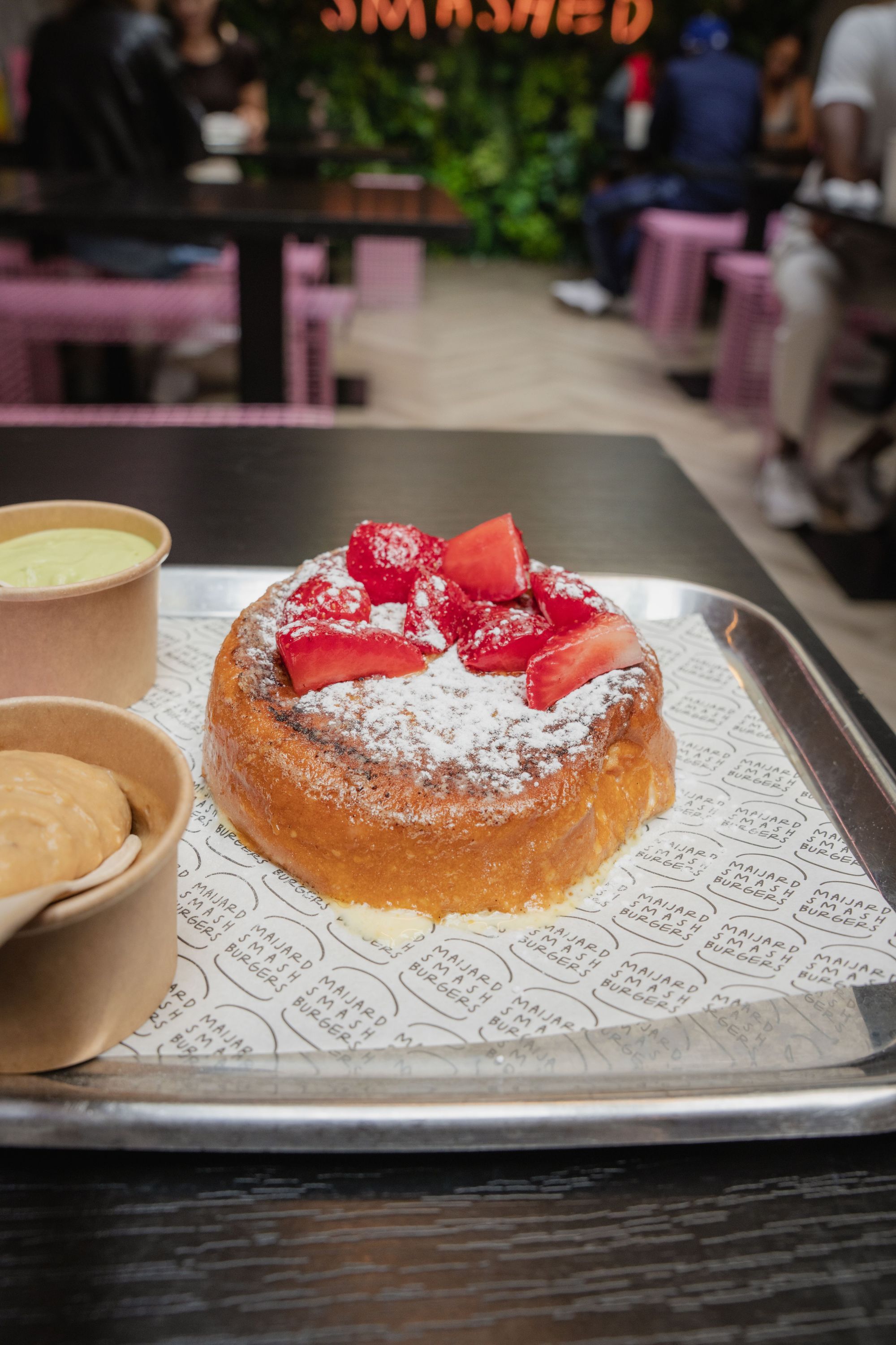 A dessert topped with fresh strawberries and powdered sugar served on a tray at Maijard Smashburgers restaurant.