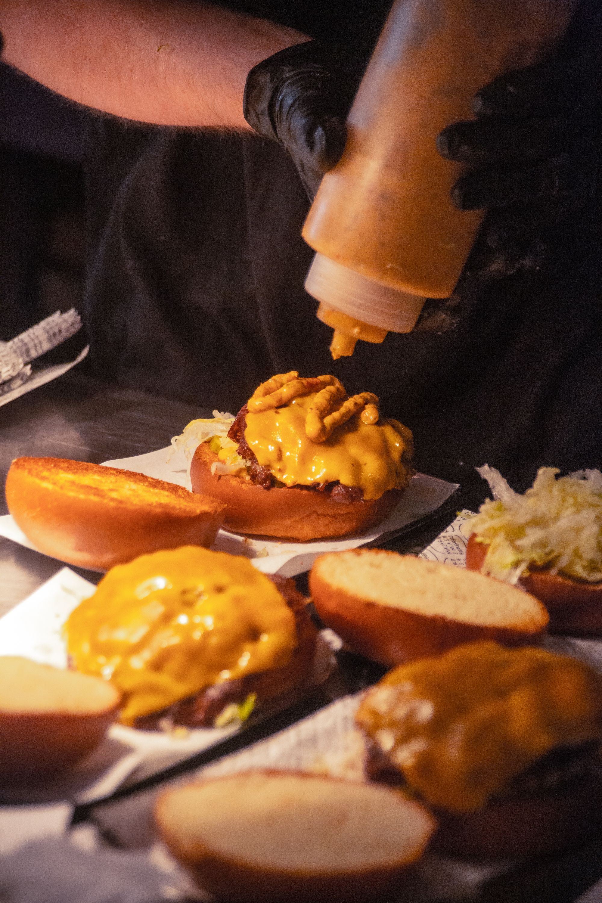 Cheeseburgers being prepared with a special sauce, featuring toasted buns and melted cheese in a burger restaurant kitchen.