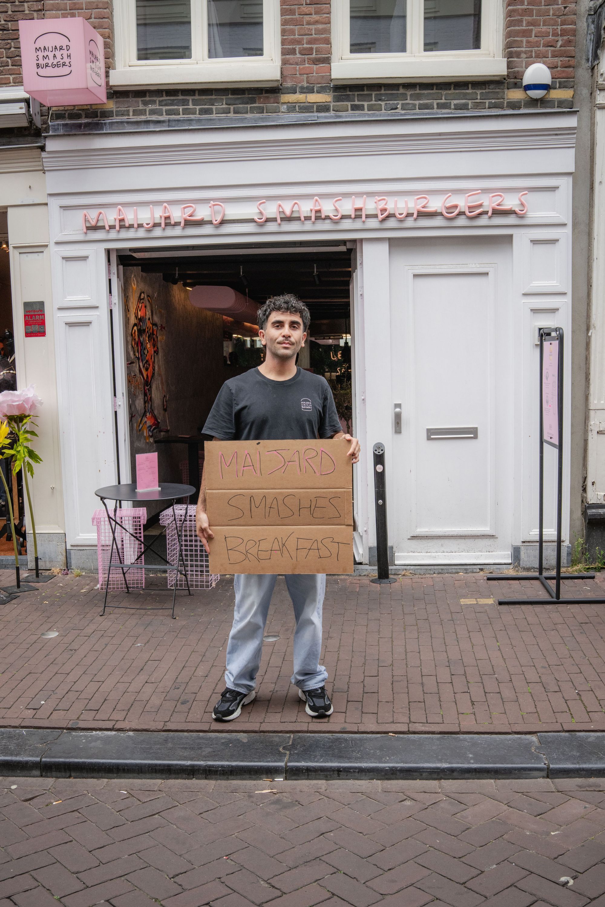 Front view of Maijard Smashburgers restaurant in Amsterdam with a person holding a promotional sign outside the entrance.